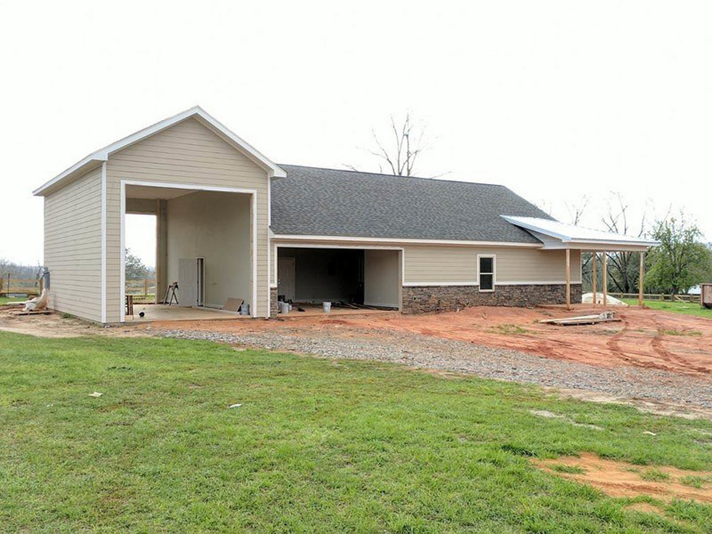 Framed house under construction with exposed plywood walls, open garage, grassy lot, and partially finished roof