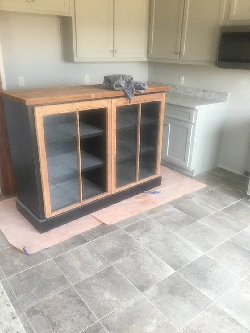 White marble countertop with grey tile floor, glass-front cabinet, and wooden surface with folded grey towel in a modern kitchen.