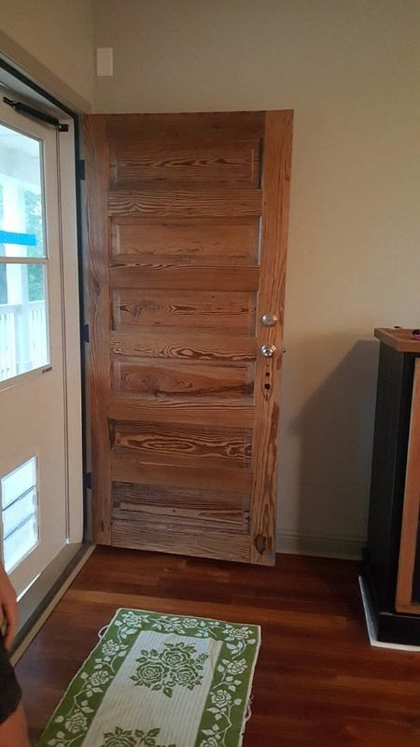 Wooden door with silver knob set in a room with hardwood flooring, green and white floral towel, green and white rug, and black rectangular object with brown surface.