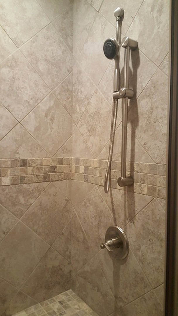 Walk-in shower with large gray wall tiles, glass enclosure, and chrome hand shower mounted on tile wall