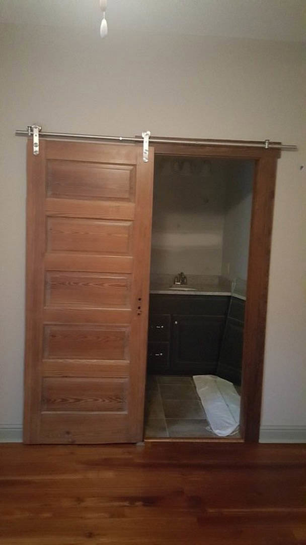 Bathroom with sliding wood door, white towel on light tile floor, built-in cabinetry and neutral walls.