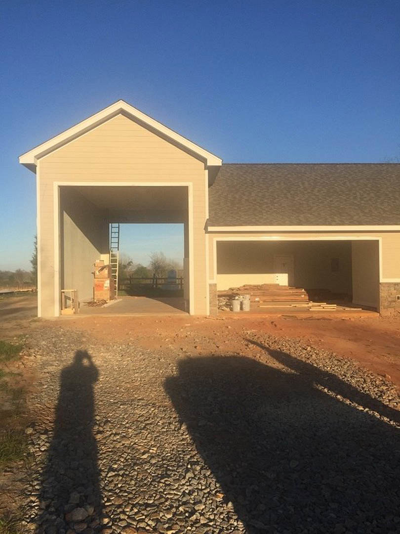 Framed garage with open door, exposed wood beams, construction ladder, rocky ground, shadow of person, unfinished exterior walls