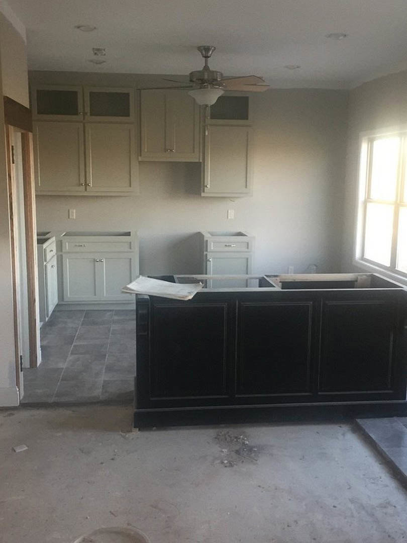 Modern kitchen featuring a ceiling fan, black and white cabinetry, grey tile flooring, white walls, and a window above the countertop