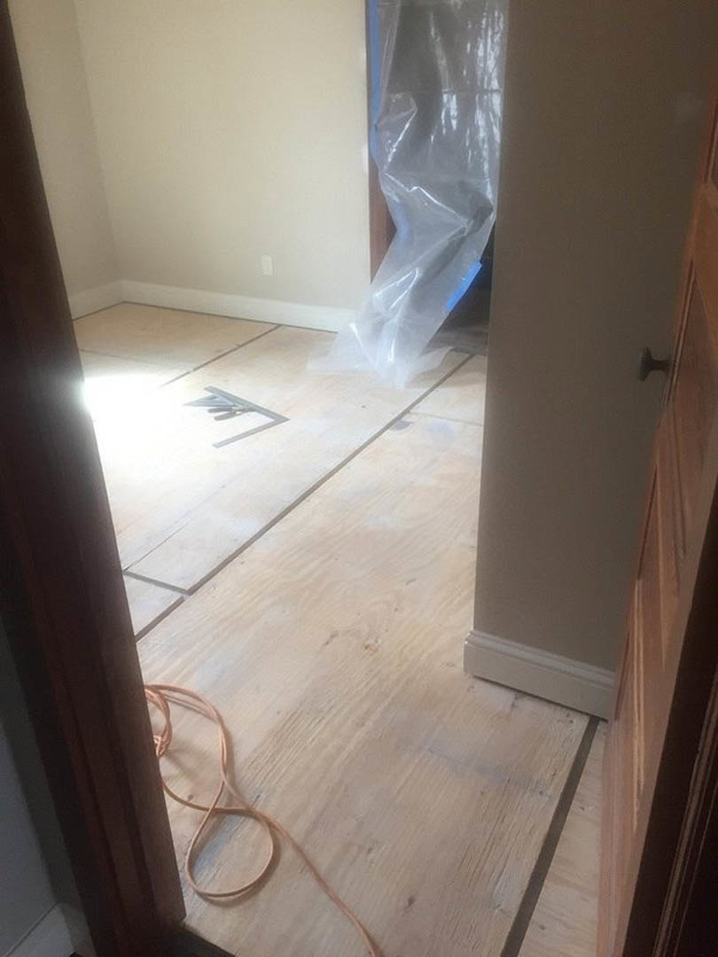 Wood floor room with scattered tools, plastic bag sealed with blue tape, string on table, close-up wire, white surface, and door knob on plaster wall