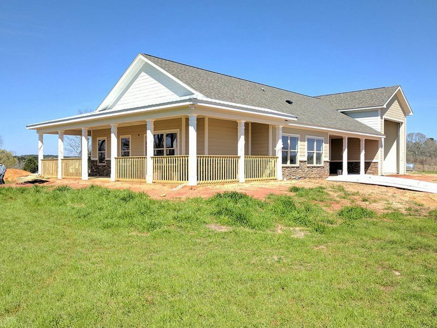 Front porch with white pillars, gray roof, large windows, manicured lawn, and white fence under blue sky