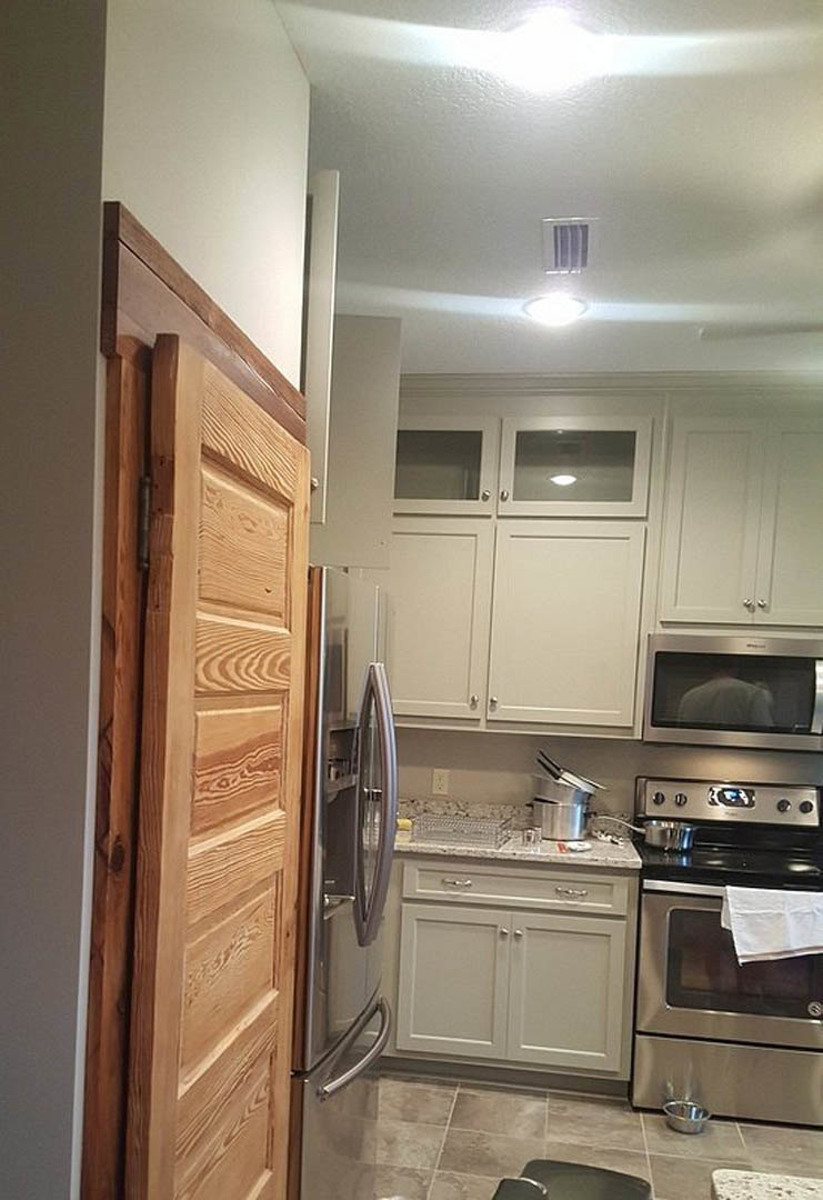 White kitchen cabinets with marble countertops, wooden door, black surface with white towel, stainless steel oven, and light walls.