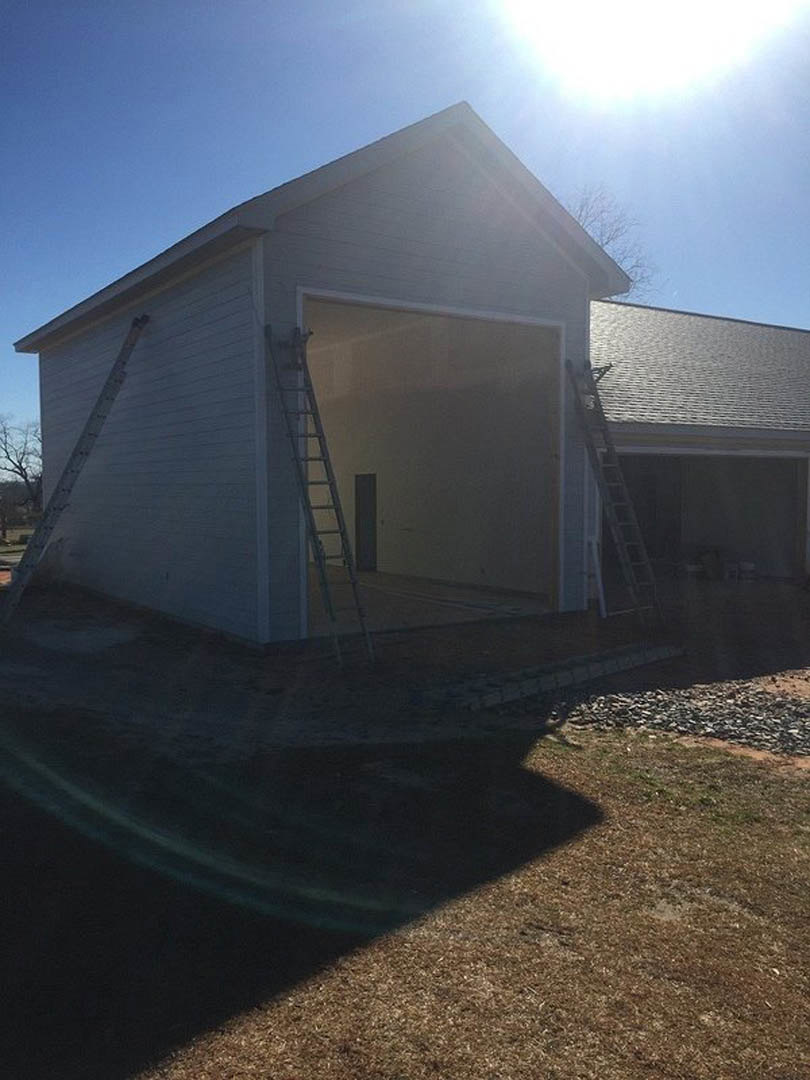 Modern home exterior with white siding, large windows, and a metal ladder leaning against the wall; blue sky with scattered clouds overhead, grassy lawn in foreground, building
