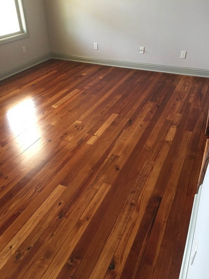 Wood plank flooring with natural finish, white walls featuring electrical outlets, sunlight streaming through a window, and a close-up view of a door in a modern interior room