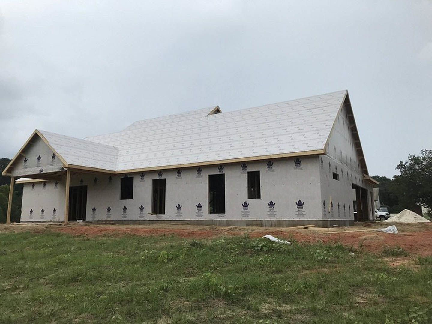 Modern custom home under construction featuring multiple large windows, unfinished exterior walls, green grass lawn, concrete foundation, and construction materials including a