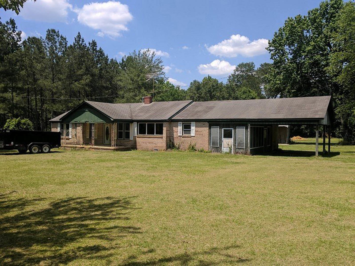 Red brick house with white-framed windows, expansive green lawn, mature trees, and partly cloudy sky