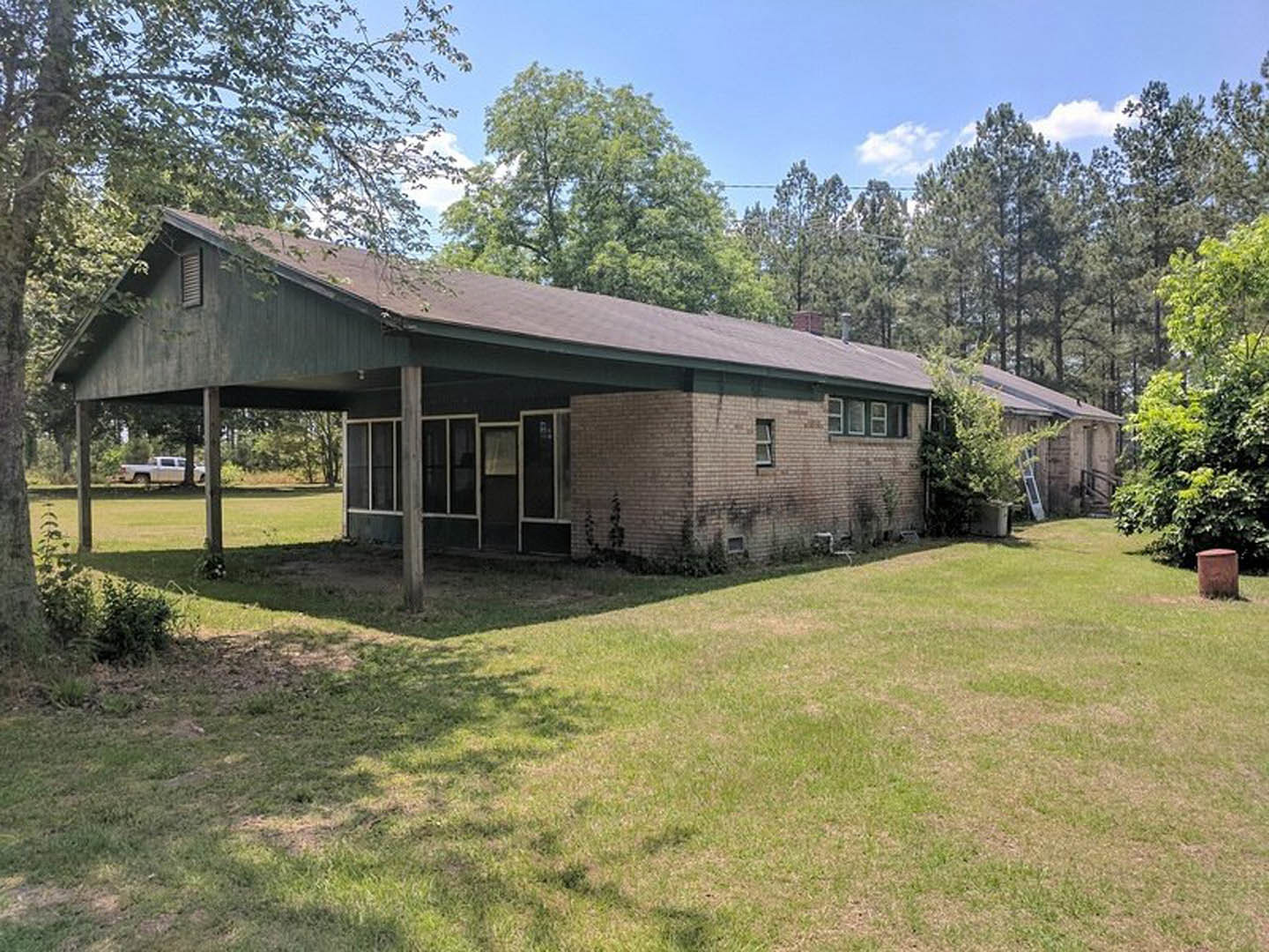 Two-story house with white siding, covered front porch supported by columns, manicured green lawn, mature trees, and blue sky in background
