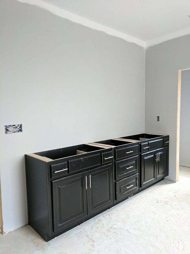 Black kitchen cabinets with drawers against a white wall, light-colored flooring, and minimal decor in a modern kitchen