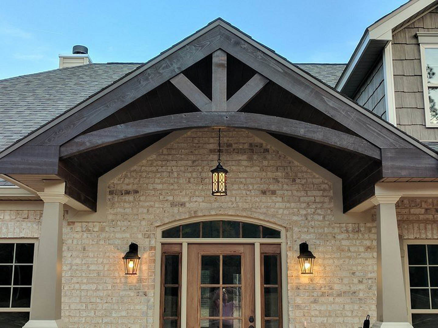 Modern home exterior with wood front door, large windows, light-colored siding, and a person standing near the entrance