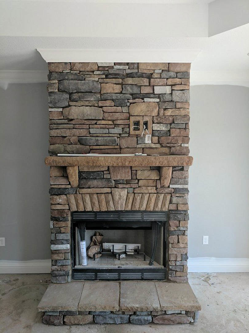 Stone fireplace with brick surround, wood-burning stove, hearth bench, and fire screen in a living room with grey walls and white trim