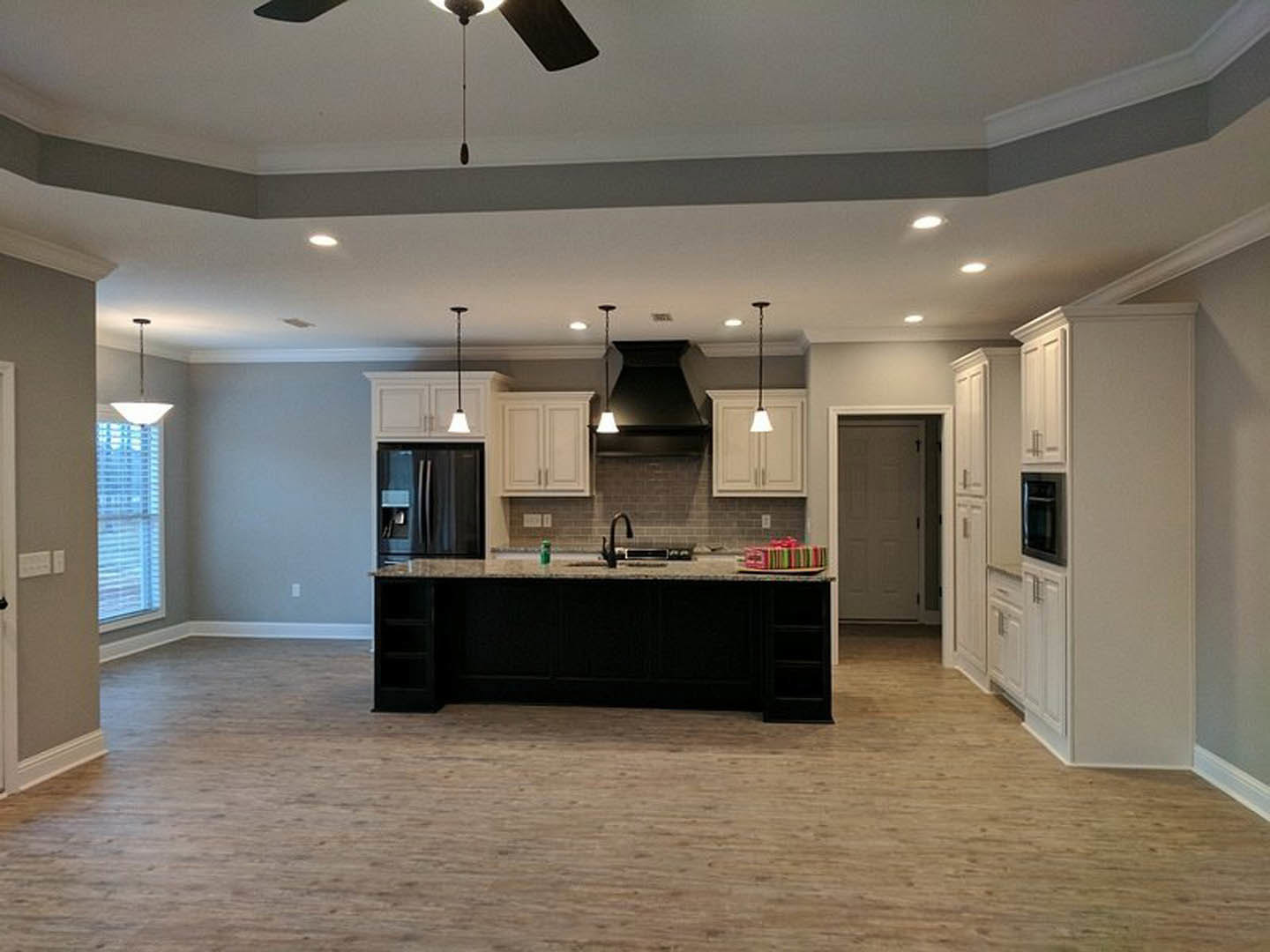 Open kitchen and dining area featuring wood flooring, black accent wall, square-patterned white door, stainless steel refrigerator, light-colored countertops, cabinetry, ceiling