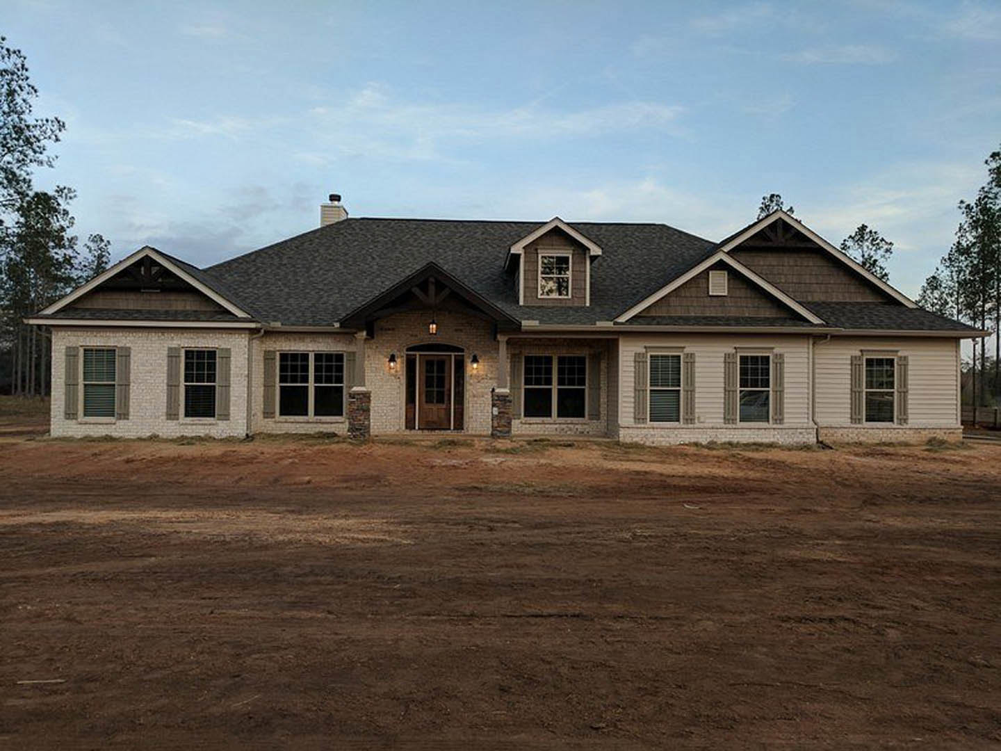 Modern house with black roof, white-framed windows, and unfinished dirt yard under cloudy sky