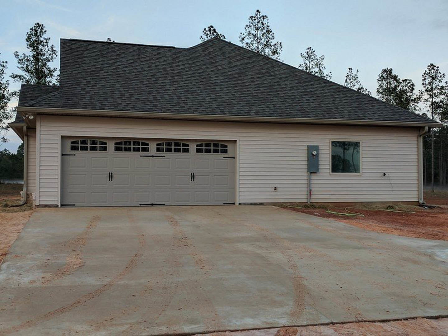 Two-story house with attached garage, gray siding, shingled roof, garage door with upper windows, concrete driveway, large front window reflecting nearby trees, Plattsburgh Air
