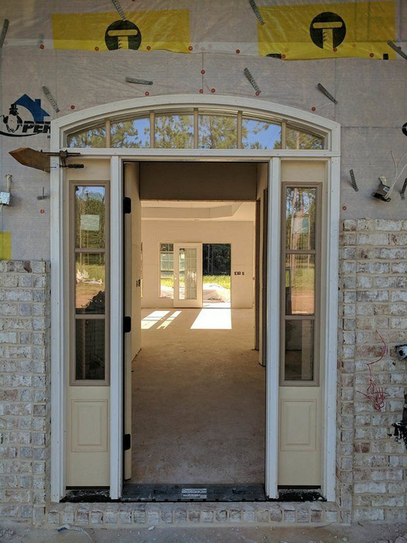 White front door with glass panels set in a red brick wall, brushed metal handle, and yellow house number plaque mounted beside the entry.