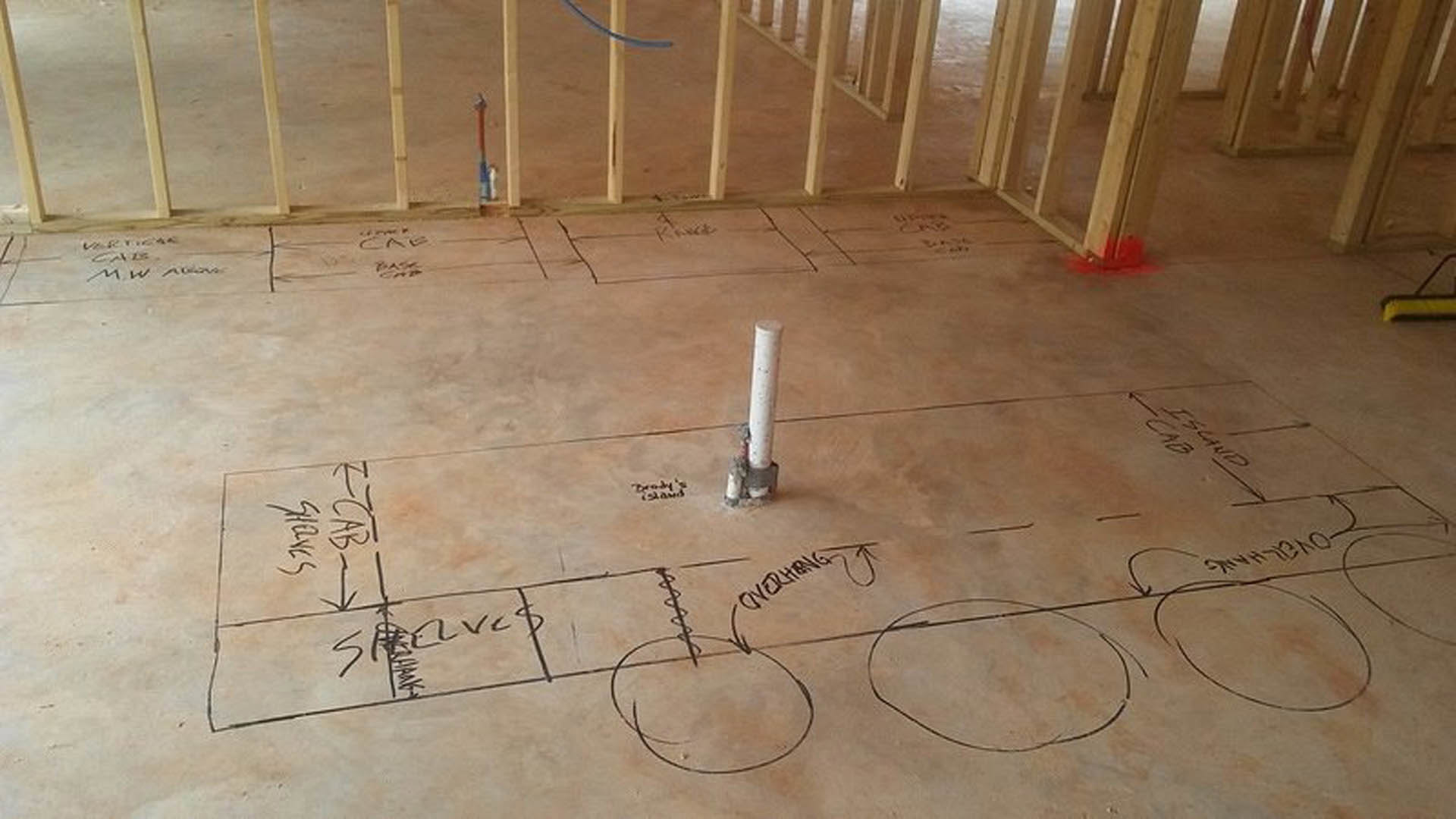 Concrete floor with hand-drawn circles and lines, white pipe with visible crack, black text markings, and scattered construction materials in unfinished interior space