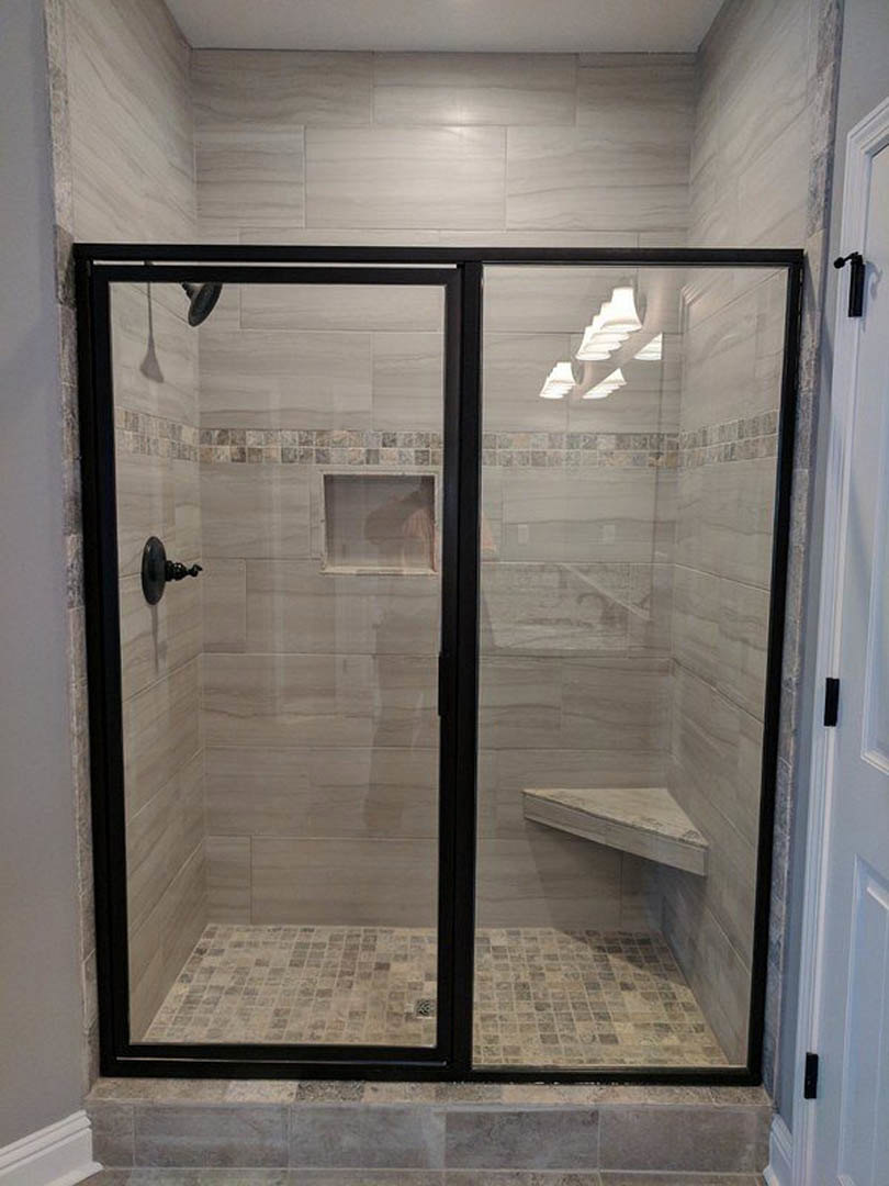Walk-in shower with clear glass doors, marble tile walls, built-in bench, and chrome shower head