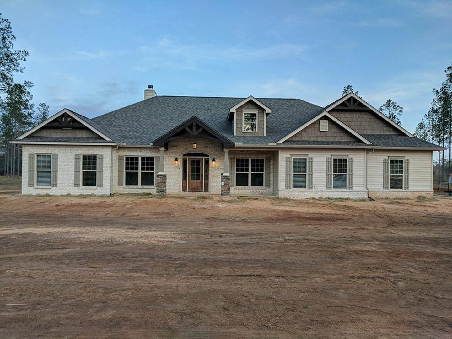 Partially built house with white-framed windows and door, surrounded by exposed dirt and construction materials, under a cloudy sky