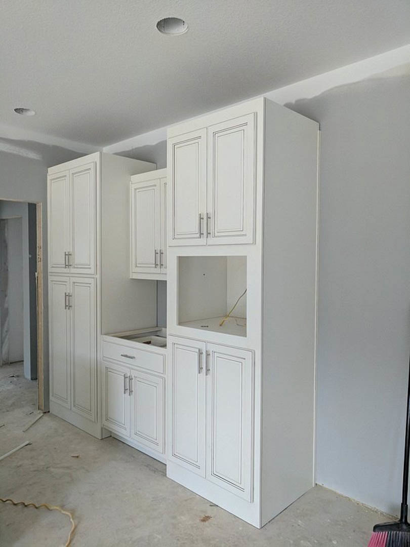 White shaker-style kitchen cabinets with silver handles, light wood flooring, white walls, and recessed ceiling lighting