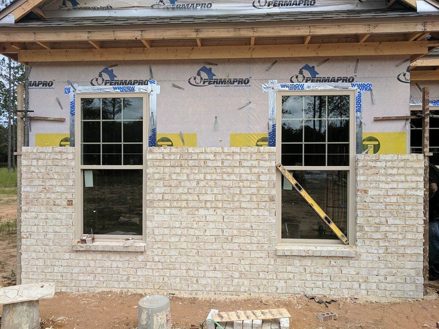 White brick exterior wall with two windows, white frames, and a yellow ladder leaning against one window
