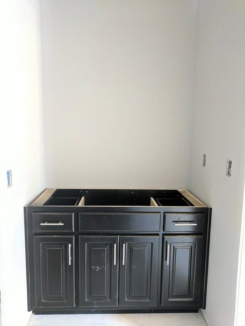 Matte black kitchen cabinet with drawers and silver hardware, set against a white wall with light-colored countertop
