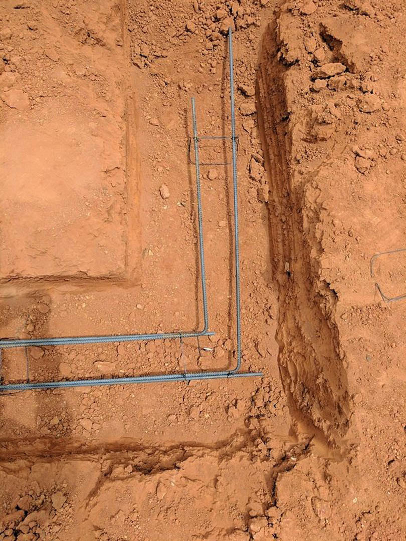 Beige and brown soil trench with exposed metal pipes, brick exterior wall in background, outdoor construction site