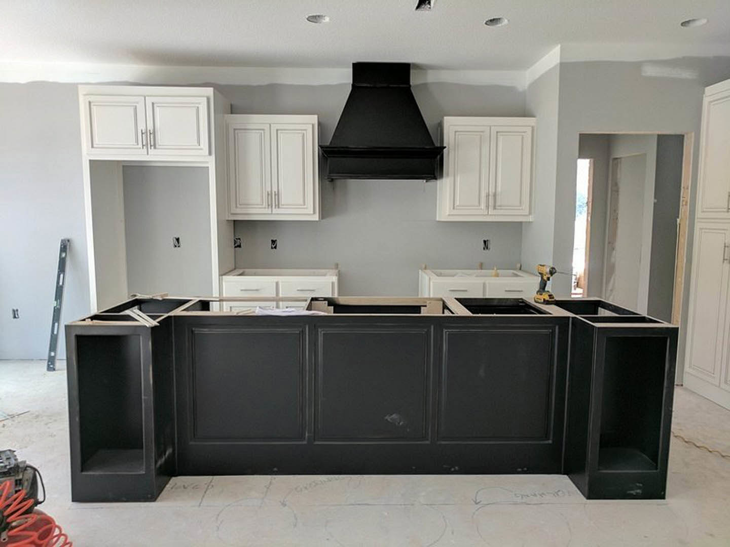 Modern kitchen featuring white upper cabinets, black lower cabinets, black vent hood above white cabinetry, white walls, and a black shelf; stainless steel appliances and light