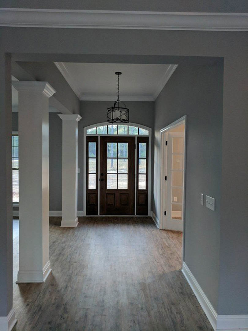 Hallway with wood flooring, white columns, brown door with glass panes, ceiling chandelier, and chain hanging from ceiling