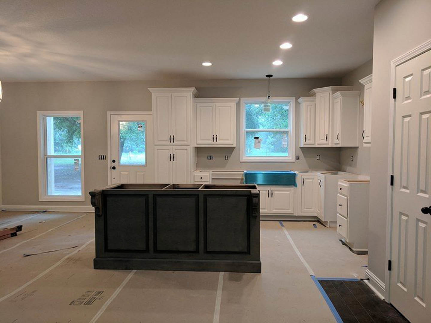 White kitchen cabinets and black island with black panel, black tile floor with blue trim, window showing outdoor view, white door visible in foreground.