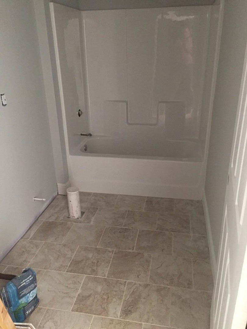 Bathroom with freestanding tub, light tile flooring, white plaster walls, and a decorative white pillar with black dot accents