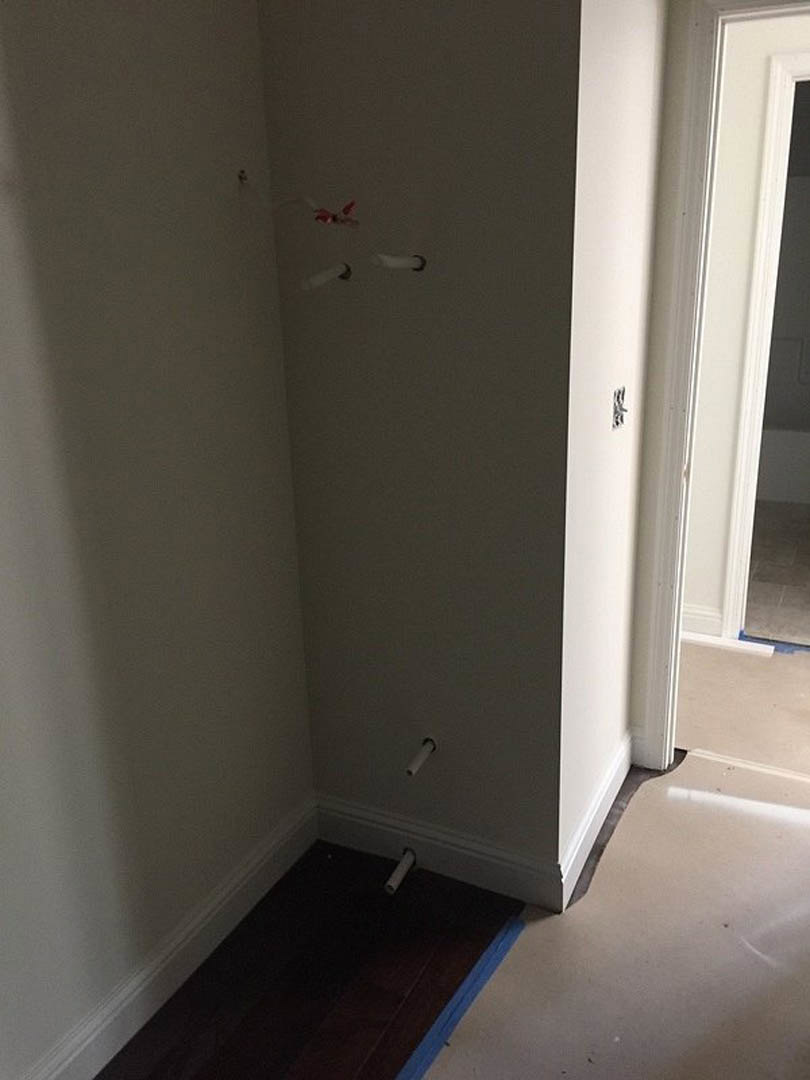 White plaster wall with exposed metal pipes, white floor, and blue mat in a residential interior.