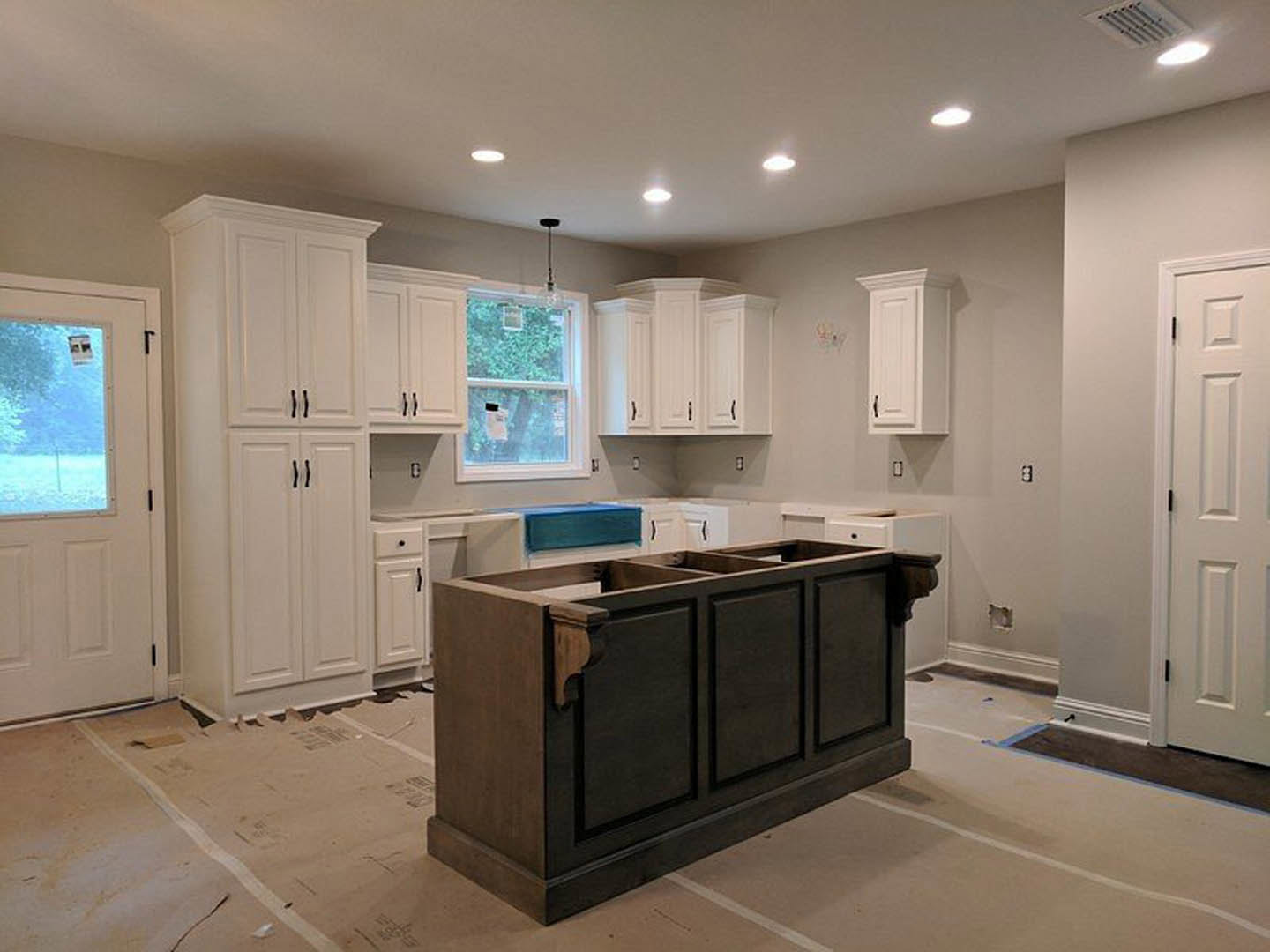 White kitchen with shaker cabinets, light stone countertop, stainless sink, tile backsplash, and vented ceiling above window with white trim.