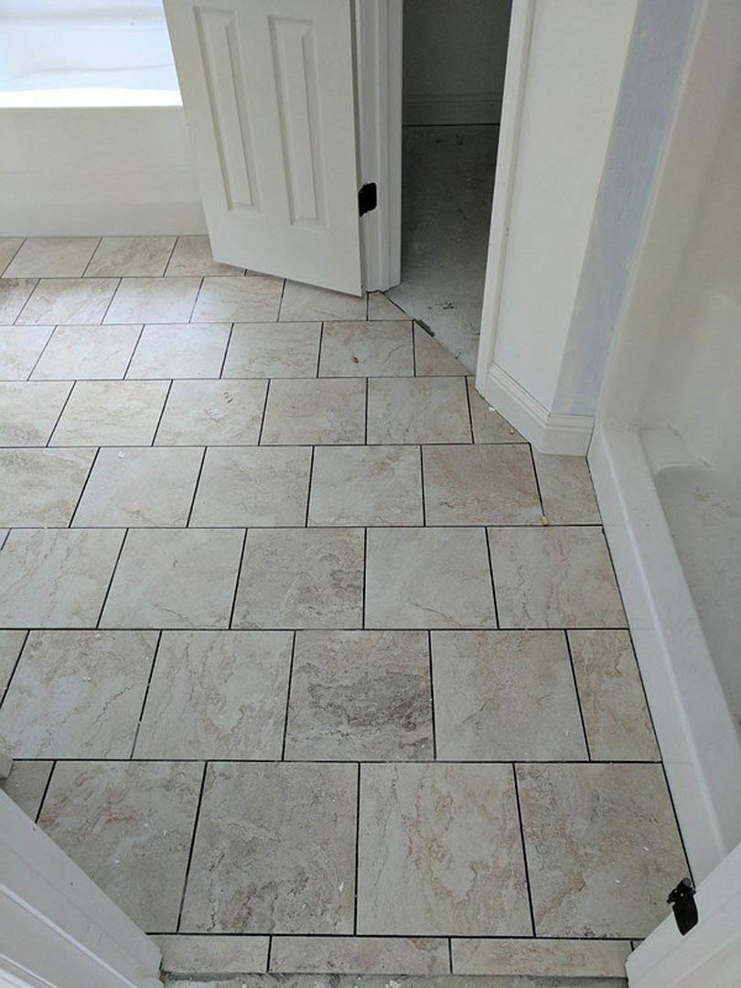 Grey tile flooring with a white door open, showing detailed tile pattern and smooth plaster walls