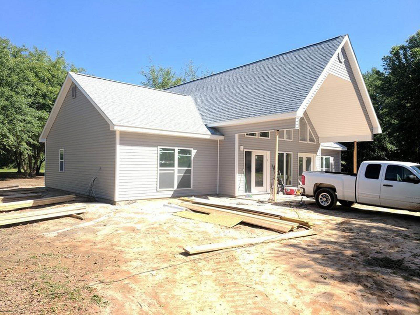 White pickup truck parked in driveway of partially constructed home with white-framed windows, attached garage, and mature trees in background