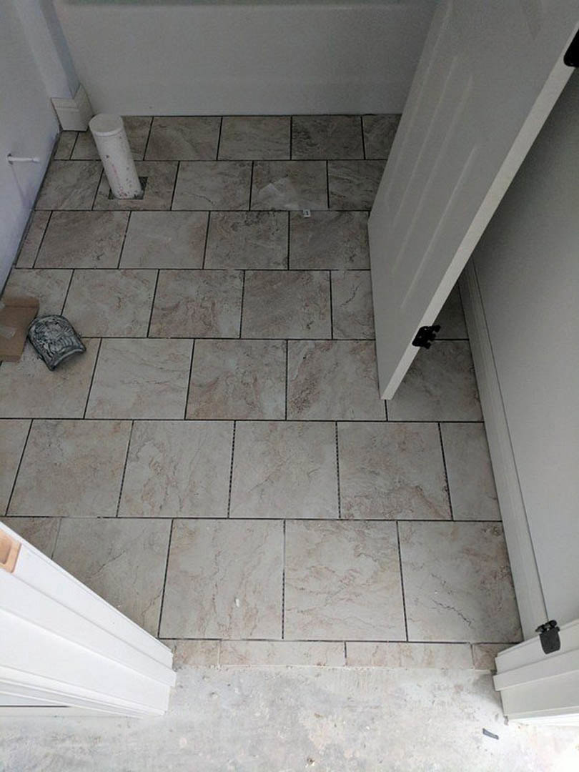 White tile floor with open white door, grey cylindrical object near threshold, plaster walls, marble and concrete finishes visible.