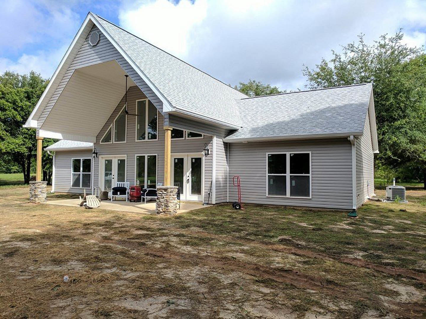 Two-story home with covered porch, white-framed windows, stone pillar, and manicured lawn; Robert Frost Farm visible in the background under partly cloudy sky