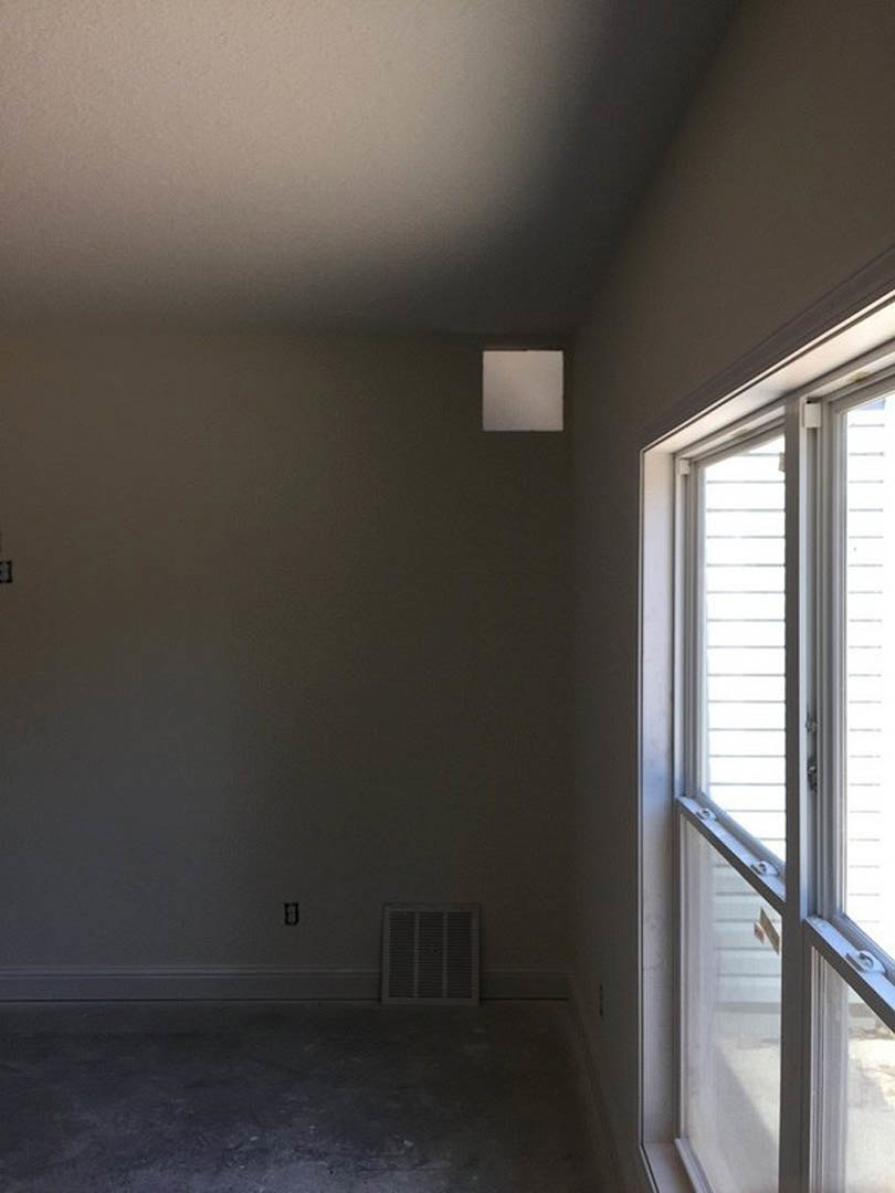 Modern room with plaster walls, large window with black trim, wall vent, dark polished concrete floor, and minimal white square light fixture.