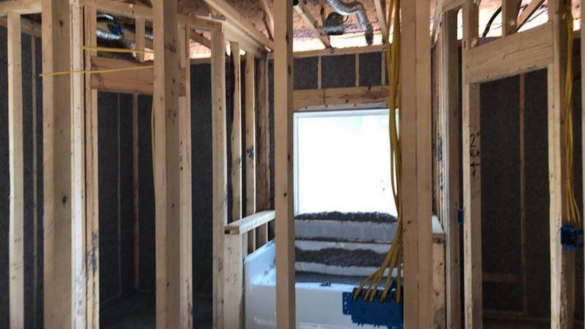 Freestanding white bathtub beneath large window, natural light highlighting wood plank flooring and exposed ceiling beams