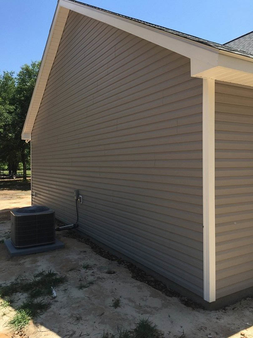 Modern house exterior with light-colored siding, black garage door, and white pillars; black outdoor heater with round top and cord mounted near entrance; clear sky and landscaped