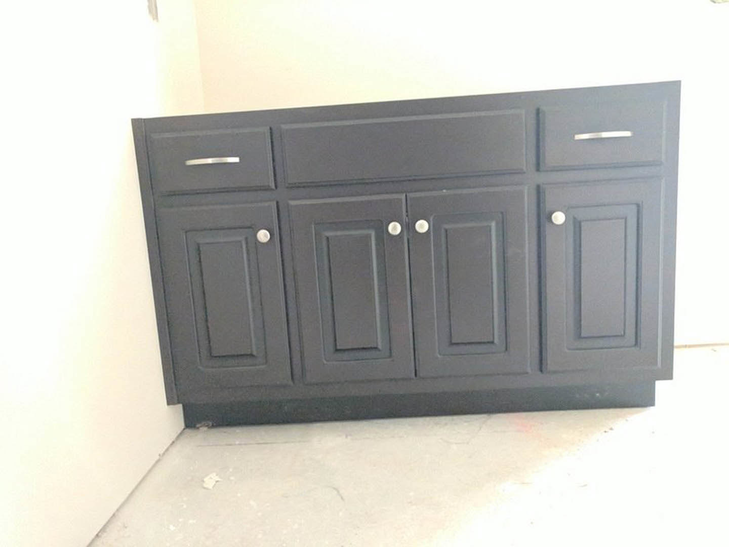 Matte black cabinet with minimalist drawers against a white wall, white floor, and white door in a modern interior room