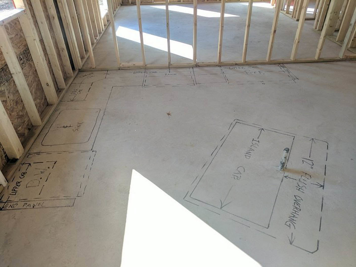 White floor with black marker drawings, wooden framing along the edges, natural daylight illuminating the interior room.