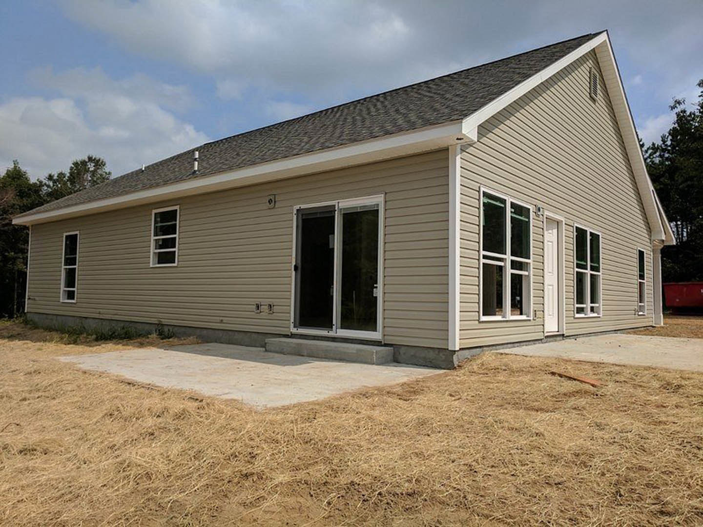 Modern house exterior with white siding, black-framed glass door, large windows, covered patio, and green lawn under partly cloudy sky