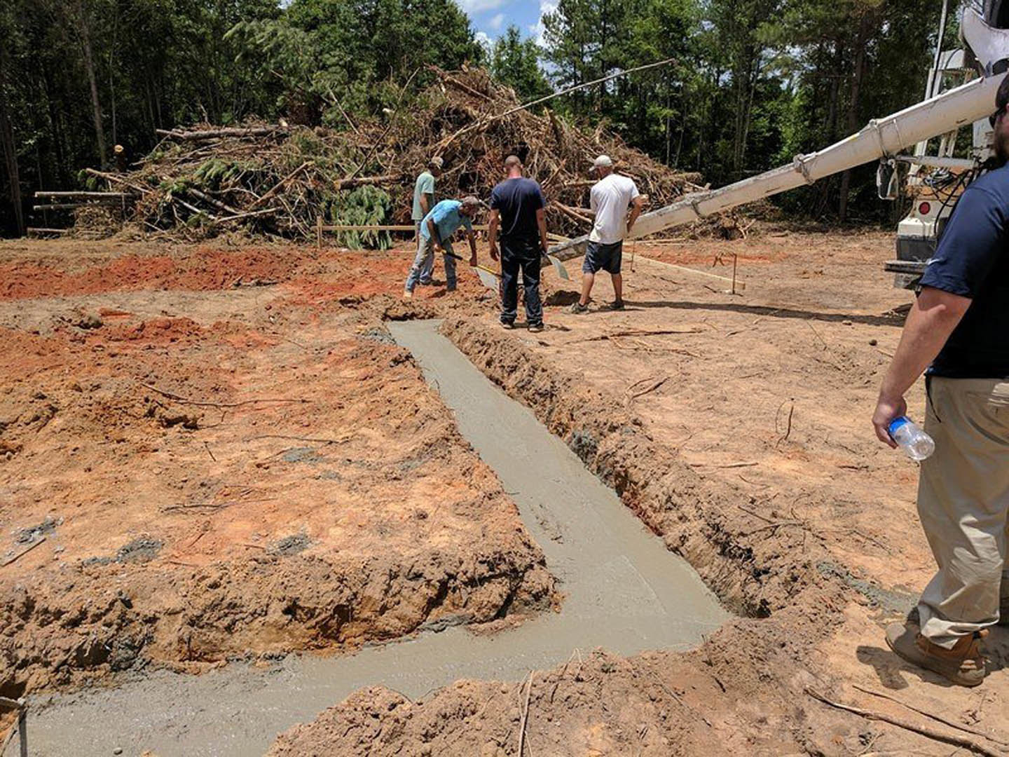 Men working outdoors on a custom home construction site, digging in soil and wearing casual clothing, with trees and sky in the background