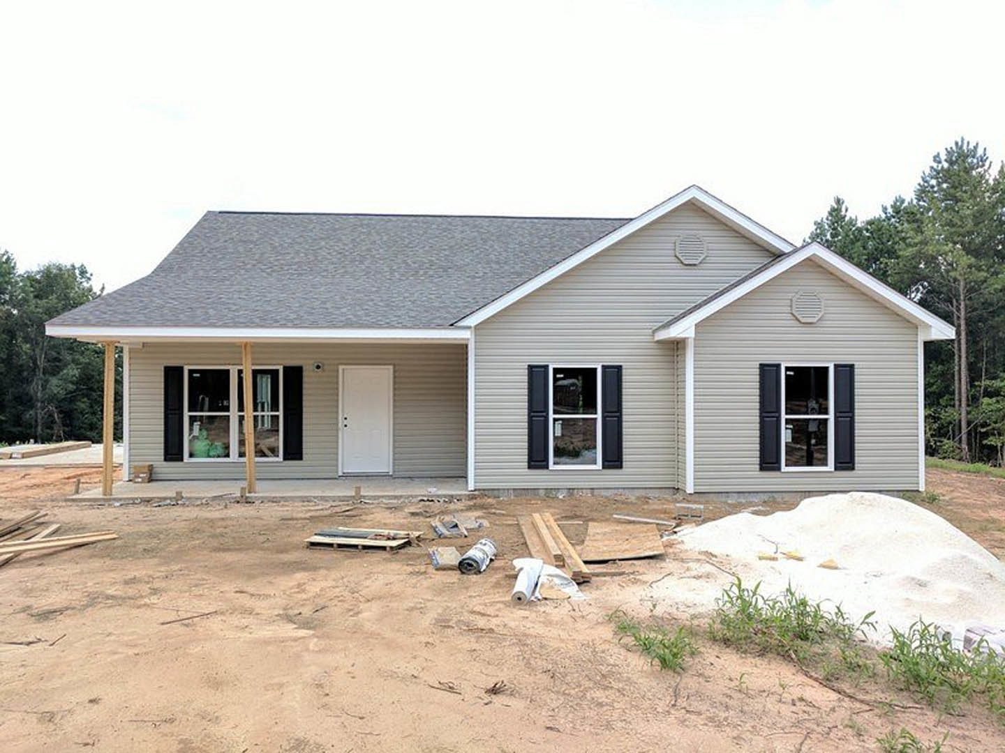 Partially built house with white siding, white framed window, white door with black hardware, exposed dirt yard, and construction debris on the ground