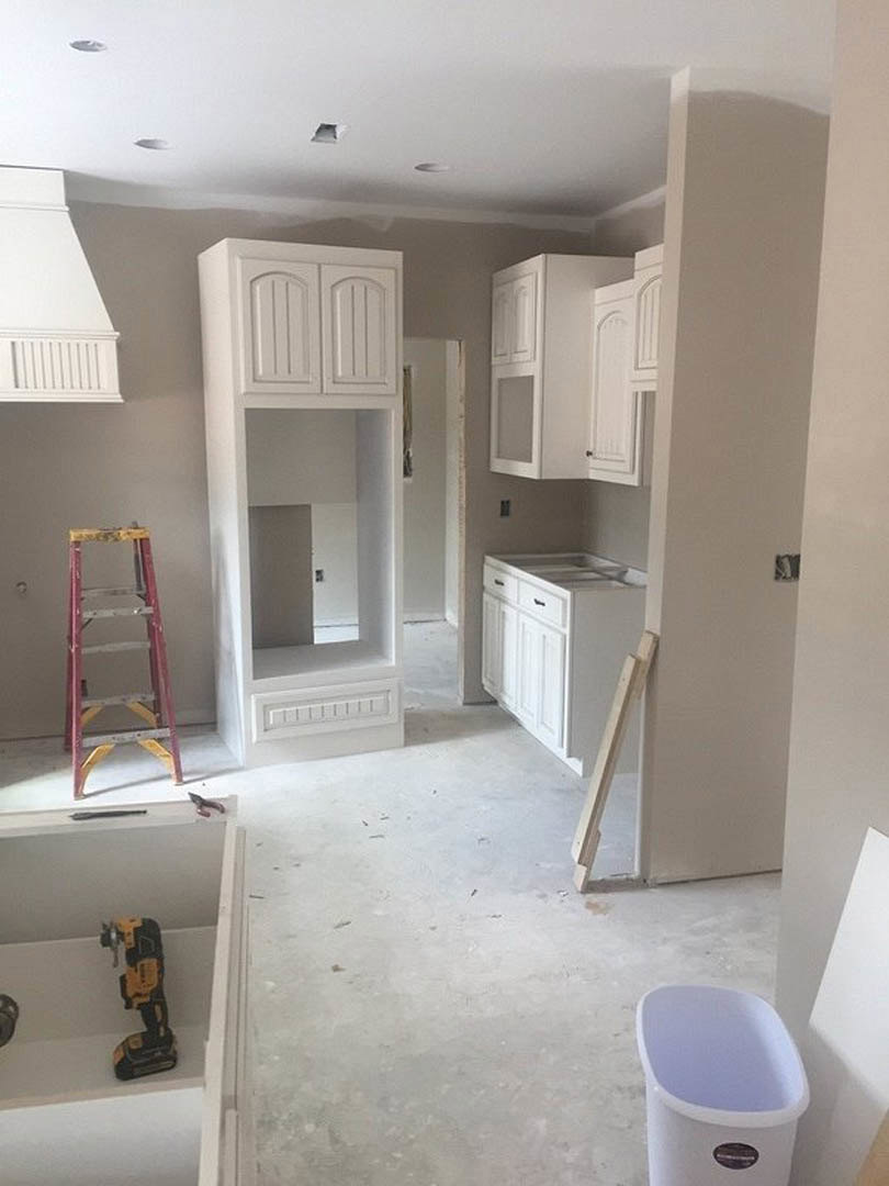 Kitchen under construction with unfinished white plaster walls, exposed cabinetry, tile flooring, a ladder leaning against the wall, white trash can with sticker, and wooden leg