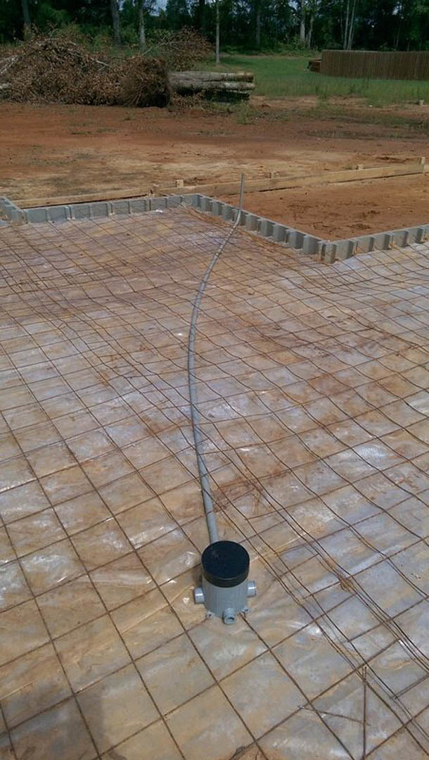 Wire mesh laid across flagstone ground outdoors, with a metal pipe on a tarp, nearby fire hydrant, and tree trunk in the background.