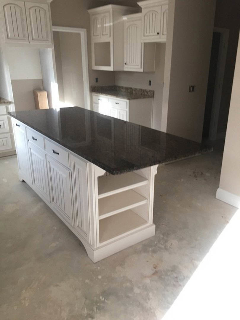 Kitchen island with polished black granite countertop, white cabinetry with vertical panel doors, stainless steel sink, and light wood flooring